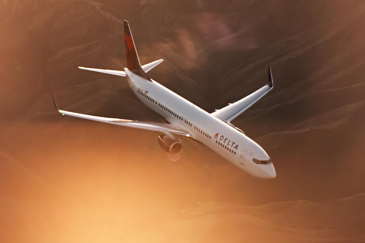 A 737-900 flies while a mountainous terrain displays in the distance.
